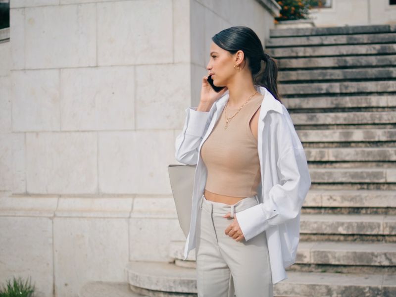Devojka u beloj košulji, krem majici i pantalonama razgovara na telefon