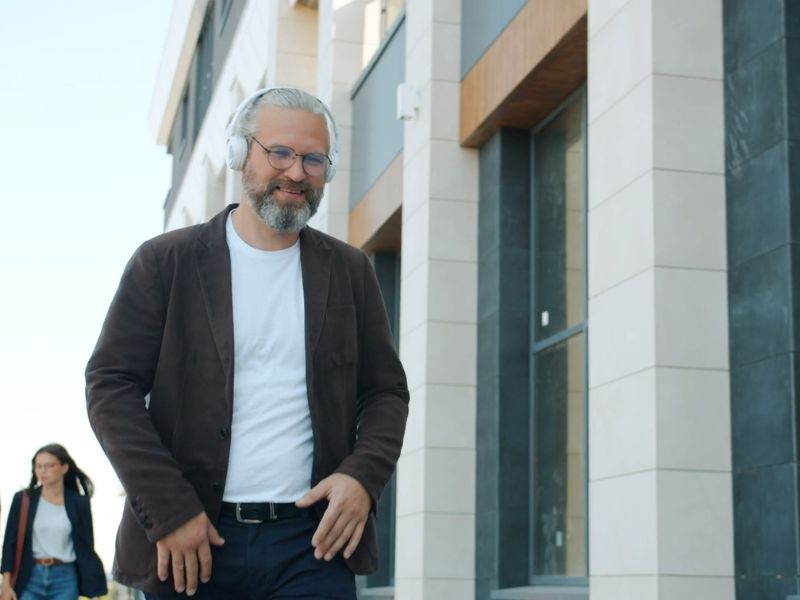 Muškarac u opuštenoj beloj majici i tamnom sakou sa slušalicama na ušima